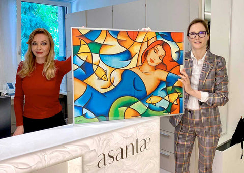 Künstlerin Ekaterina Moré übergibt ein Originalgemälde an eine Frauenärztin – sinnliche Auftragskunst für die Arztpraxis.