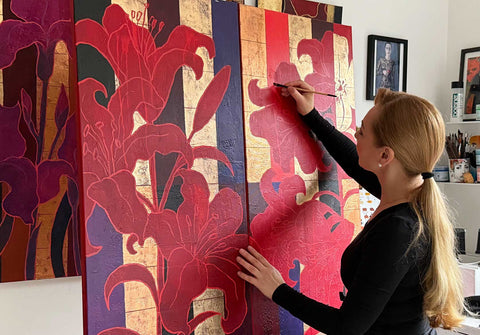 Künstlerin Ekaterina Moré im Atelier malt ein großformatiges abstraktes Blumenbild mit Lilien und Goldakzenten – ein Originalgemälde voller Emotion fürs Wohnzimmer.